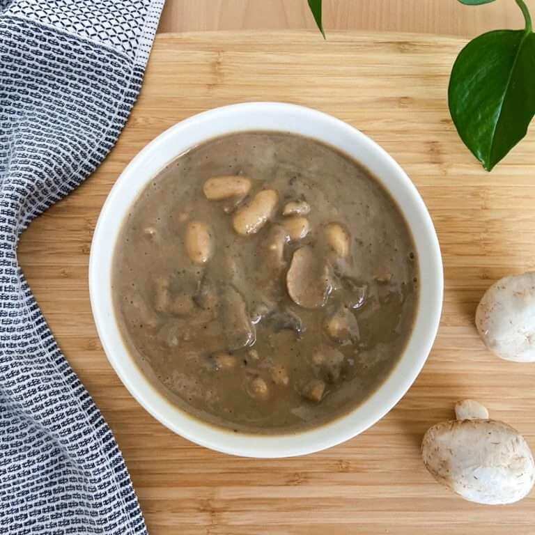 White bean and mushroom soup in a white bowl on a bamboo chopping board.