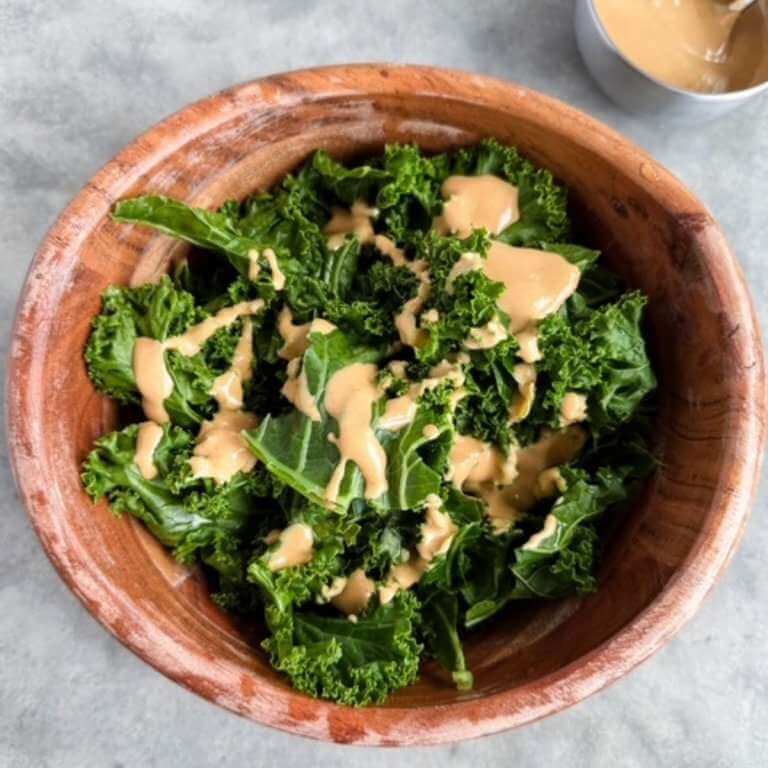 Steamed kale in a wooden bowl drizzled with creamy tahini sauce.