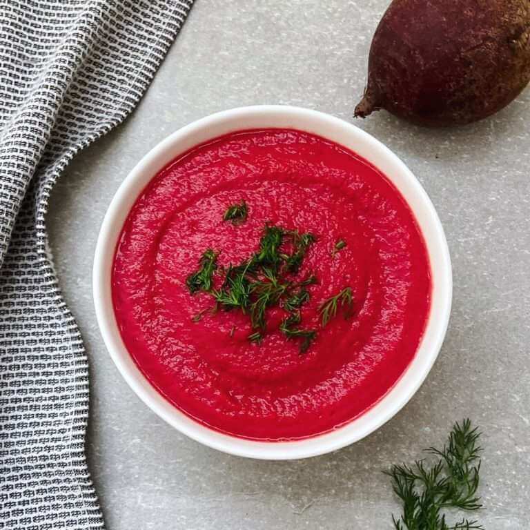Liver detox soup in a bowl with a tea towel, raw beet and sprig of dill beside the bowl.