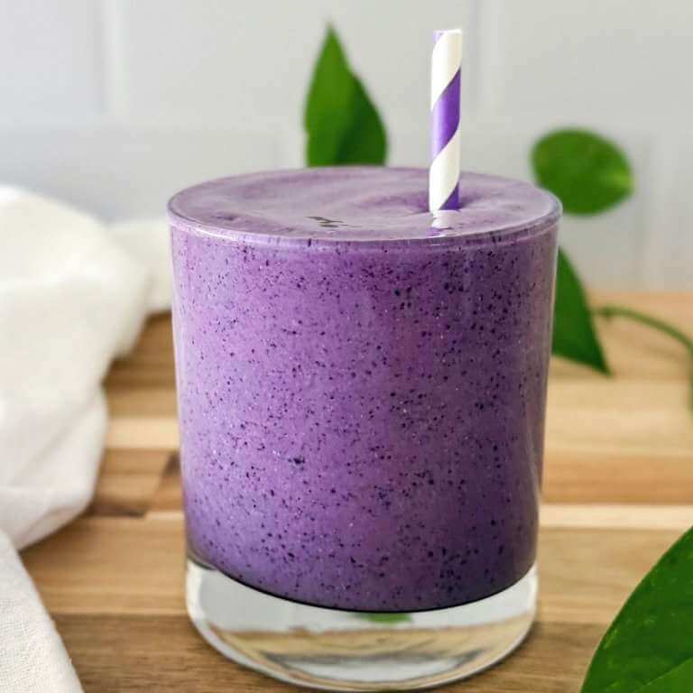 Creamy blueberry smoothie in a glass with a straw on a wooden surface