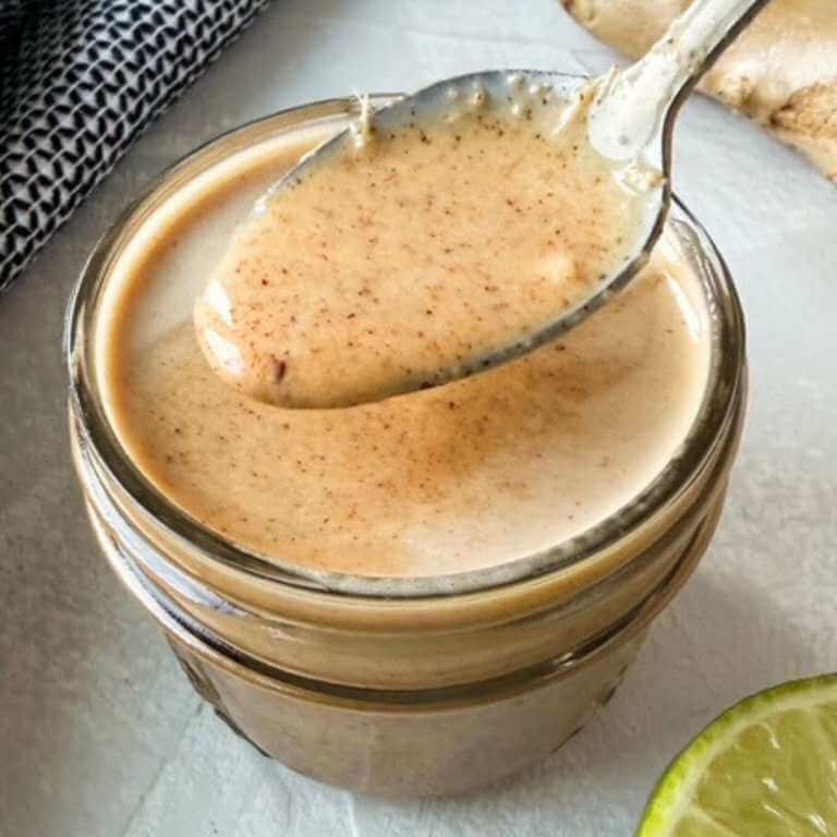 Creamy almond butter lime dressing in a jar with a spoon lifting the thick dressing above it