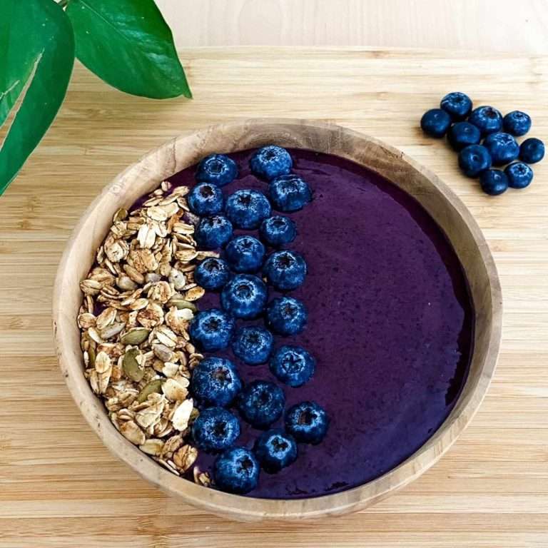 Low fodmap acai bowl in a wood bowl topped with low fodmap granola and fresh blueberries