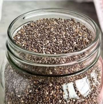 Chia seeds in a glass jar on a counter with a pink tea towel beside it.
