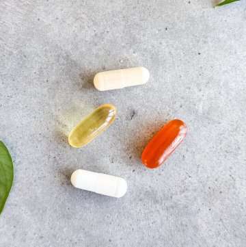 Capsules in different colors arranged on a light surface with a green leaf in the corner, representing daily vitamins and supplements.