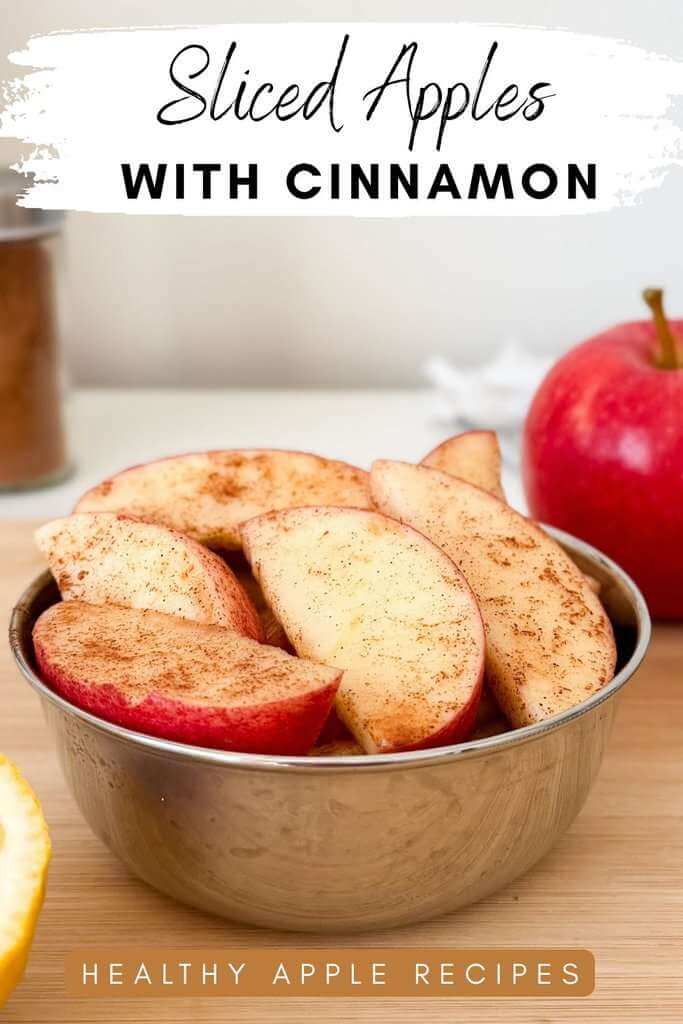 Sliced apples with cinnamon and fresh lemon juice in a bowl with a red apple and lemon in the background.
