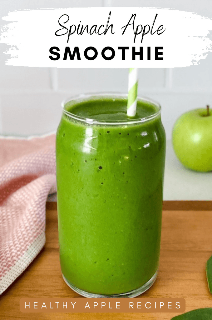 Green smoothie in a glass with a stiped green straw and pink towel and green apple in the backdrop.
